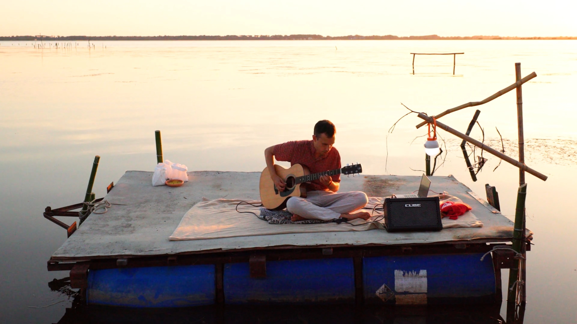 man playing guitar on a platform floating on a lake